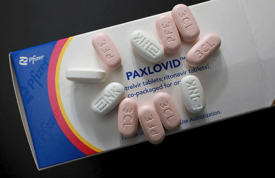 closeup of pink and white Paxlovid pills and a paxlovid box